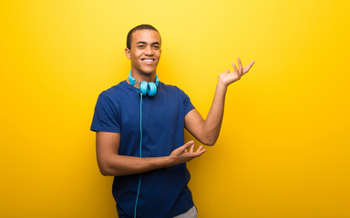 African american man with blue t-shirt on yellow background extending hands to the side for inviting to come