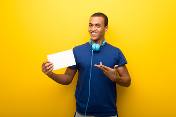 African american man with blue t-shirt on yellow background holding an empty white placard for insert a concept