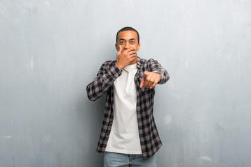 Young african american man with checkered shirt pointing with finger at someone and laughing