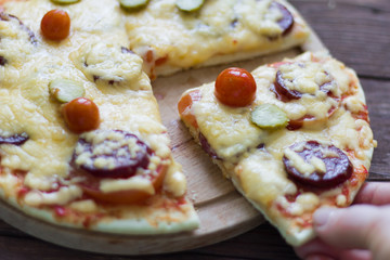 homemade hot pizza with salami and cheese, pickles and tomatoes on wooden background, ready to eat