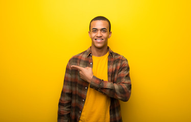 Young african american man on vibrant yellow background pointing to the side to present a product