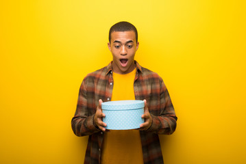 Young african american man on vibrant yellow background holding gift boxes in hands