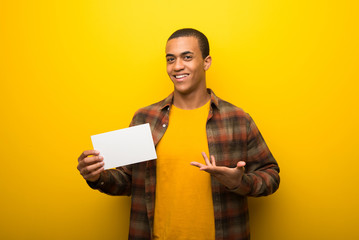 Young african american man on vibrant yellow background holding an empty white placard for insert a...