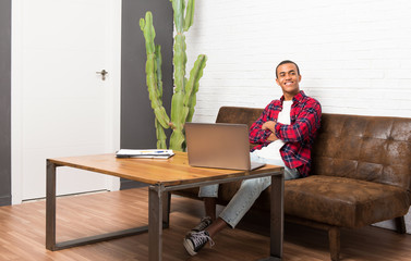 African american man with laptop in the living room keeping the arms crossed in frontal position