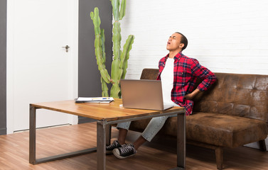 African american man with laptop in the living room suffering from backache for having made an effort