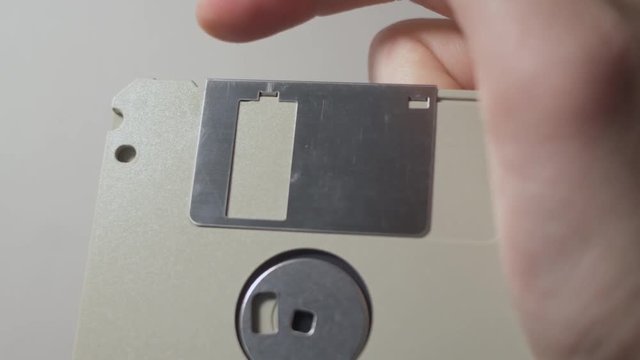 The metal protective cover on a 3.5 inch floppy disk being pulled back, revealing the black disk inside.