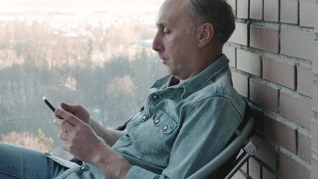 A middle aged man uses a smartphone. He is studying various programs