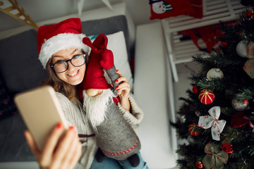 Portrait of beautiful woman with Santa Claus using cellphone near Christmas tree.