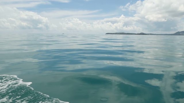 Small foamy blue waves after a boat and calm ocean in cloudy day. Idyllic tropical waterscape. The sky is reflected in the surface of the quite water of the sea. windless weather