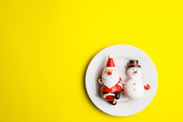 Small snowman and Small Santa Claus on white dish isolated on yellow background at Christmas...