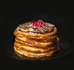 A stack of bright delicious fragrant pancakes with berries on a black background.