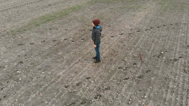 The lonely boy wanders in autumn in an empty, plowed, gray field. The croaker is looking for something in the field. The boy is running and walking.