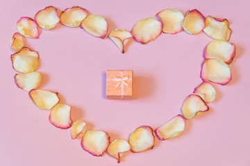 Pink gift box in frame of dried cream rose petals in heart shape
