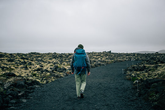 Back of traveler or hiker walking away into distance in waterproof jacket, beanie hat and backpack for camping gear. Epic grey and green moss covered icelandic landscape. adventure vibes lifestyle
