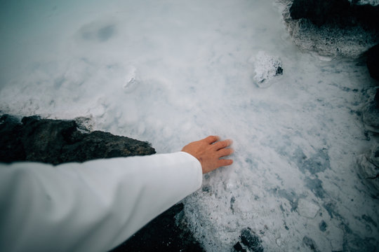 Scientist, researcher or explorer in white raincoat or doctor medical robe touches blue lagoon geothermal water. High amount of silica and sulfur research and development facility