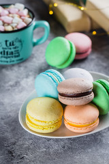 Bright macaroons and mug with hot chocolate with marshmallow on gray background from above. Colorful almond cookies, pastel colors.