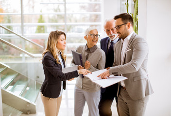 Mature and young businesswoman and a businessman standing in the office analyzing plan