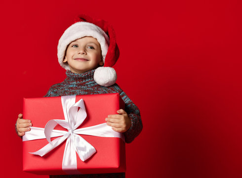 Smiling funny child in Santa red hat holding Christmas gift in hand. Christmas concept.