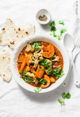 Roasted curry vegetables. Sweet potatoes, cauliflower, carrots, onions, pumpkin with curry sauce on light background, top view. Vegetarian food concept