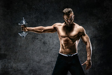 Fototapeta na wymiar Young male bodybuilder doing exercise with heavy weight dumbbells. Photo of muscular man on dark background. Strength and motivation.