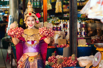 Woman wearing Thai style dress are Holding shallots in market. 