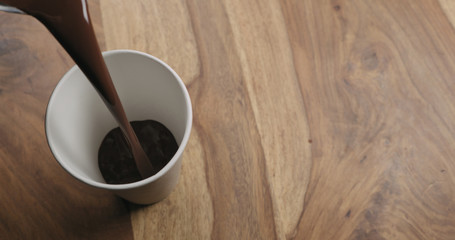 pour hot cocoa in paper cup on wood background with copy space