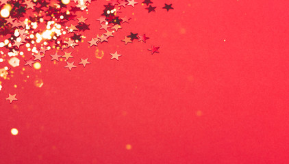 Beautiful festive red background with red metallic star shaped confetti. Christmas holidays background. Copy space for your text.