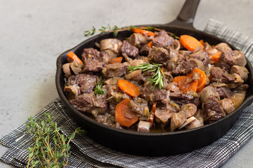 A skillet with beef bourguignon or meat stewed with sausages, carrots, garlic, onion, red wine, fresh herbs and spices.