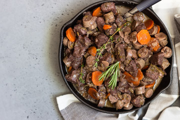 A skillet with beef bourguignon or meat stewed with sausages, carrots, garlic, onion, red wine, fresh herbs and spices.