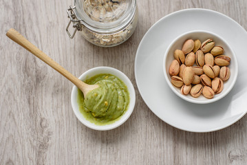 Still life of healthy and healthy food, oatmeal in a steeled jar, pistachio pasta and unpeeled salted pistachios in white plates, a wooden spoon for pasta on a light background.