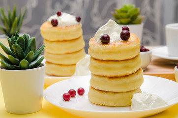 Cottage cheese pancakes with sour cream and berries on yellow ba