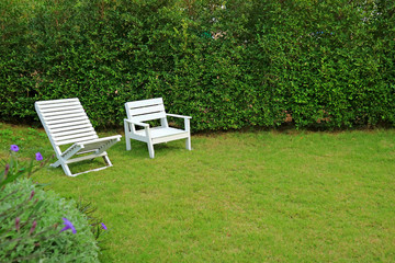 Two different type of white colored wooden chairs in vibrant green garden 