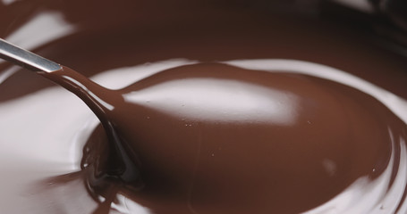 closeup pouring melted dark chocolate from spoon