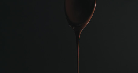 closeup melted dark chocolate dripping from spoon over black background