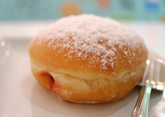 Closed up a strawberry jam filled doughnut served on white plate with fork 