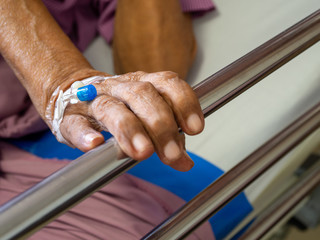 Close up hand patient elderly man hand with saline intravenous (iv) solution in hospital. patient with needle plug for use with medicine to the saline.