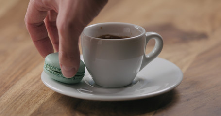 man hand put light blue macaron on saucer with coffee cup