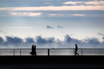 People in silhouette standing on a bridge over a sea