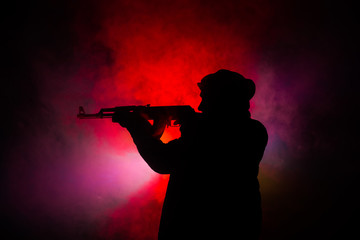 Silhouette of man with assault rifle ready to attack on dark toned foggy background or dangerous bandit in black wearing balaclava and holding gun in hand. Shooting terrorist with weapon theme decor