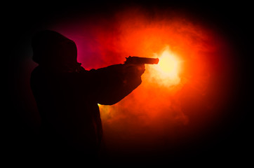 Silhouette of man with assault rifle ready to attack on dark toned foggy background or dangerous...