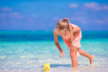 Fototapeta premium Adorable little girl playing with origami boat in turquoise sea