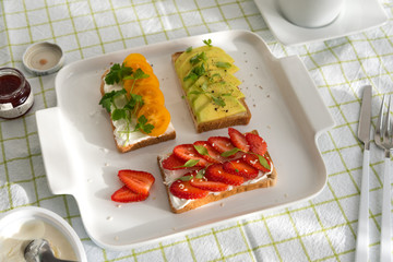 Breakfast: Toast with strawberries, avocado and yellow cherry tomatoes on a plate, top view