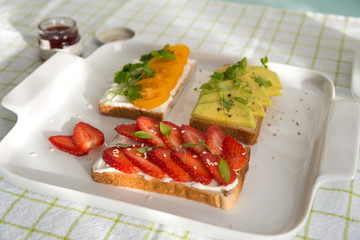 Breakfast: Toast with strawberries, avocado and yellow cherry tomatoes on a plate, top view