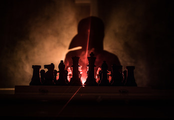 Man playing chess. Scary blurred silhouette of a person at the chessboard with chess figures. Dark toned foggy background.