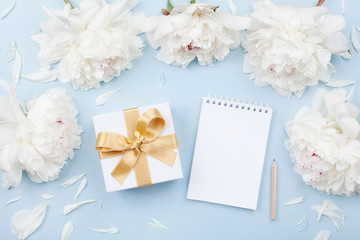 Obraz na płótnie Canvas Empty notebook and gift or present box decorated white peony flowers on pastel table top view. Flat lay composition for birthday or wedding.