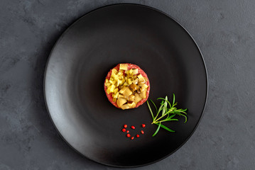 Beef tartare with pickled cucumber and marinated mushrooms on black plate. Dark background.