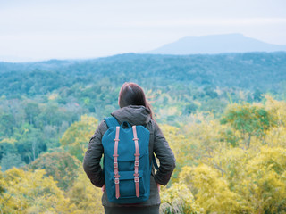 solo backpack and camping concept from backside of long hair woman in warm cloth with her bag travel, relax, happy  and see to forest and mountain in morning after sunrise