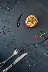 Beef tartare with pickled cucumber and marinated mushrooms on dark marble background.