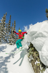 Freerider skier jumps from a rock of snow in trees in the mountains