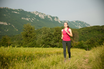 Fototapeta na wymiar Beautiful young woman workout outdoor runs across meadow in early summer